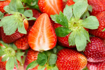 Fresh strawberries piled together with one sliced in half showcasing juicy red interior and vibrant green leaves