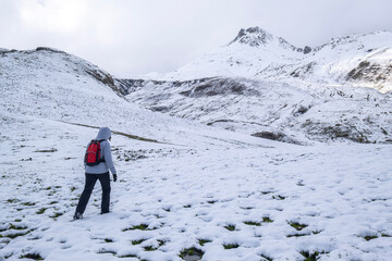 an unrecognizable woman dressed in mountain clothes and a small red backpack, crosses a snowy...