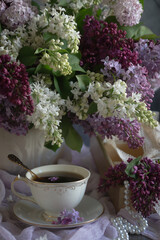 A bouquet of lilacs on the table and a cup of tea.