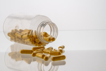 A jar with pills inside lies on a white background with reflection. Hyaluronic acid, collagen,...