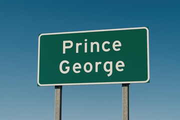 Green road sign with "Prince George" written on it stands against a bright blue sky, marking entry to the Canadian city.