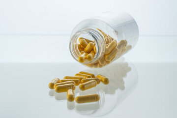A jar with pills inside lies on a white background with reflection. Hyaluronic acid, collagen,...