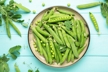 Fresh green peas in wooden bowl with pods and leaves on blue wooden background, healthy green...
