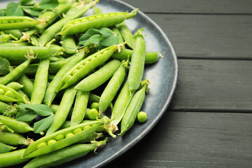 Fresh green peas in plate with pods and leaves on black wooden background, healthy green vegetable...
