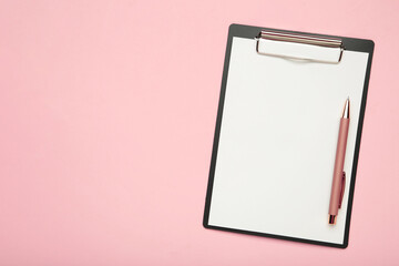Black tablet with piece of empty paper and pen on pink background.