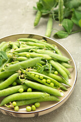 Fresh green peas in wooden bowl with pods and leaves on grey concrete background, healthy green vegetable or legume