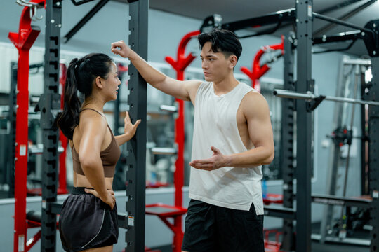Personal trainer explaining exercises to young woman in modern gym