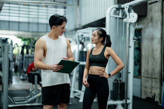 Personal trainer assisting young woman during workout at gym
