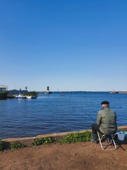 Tranquil seaside fishing scene with man sitting by water on a clear summer day
