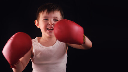 A confident child poses in a black-background studio, ready to fight. A small but fierce boxer stares ahead, ready for training or competition. Kid aged three years (3 years old)
