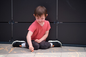 Little boy drawing with chalk on sidewalk. Happy child smiling while playing outside. Fun summer activity for preschool kid. A child aged 3 years