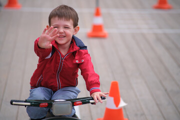 Little boy child on a tricycle waving hand. Happy kid playing outdoors in springtime. Educational activity for children's development. A child aged 3 years