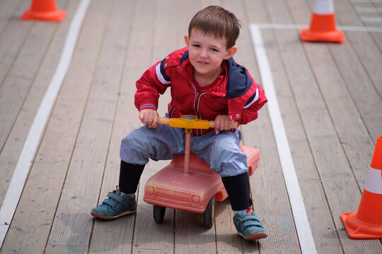 Little boy on a toy ride-on car in a marked area with orange cones, engaging in a fun outdoor activity, childhood game. A child aged 3 years