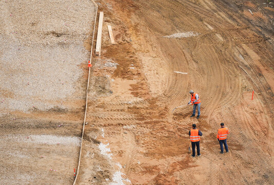 Construction workers in orange vests working with sand at a construction site. Professional shot of labor processes