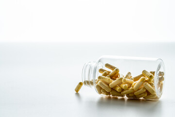 A jar with pills inside flies on a white background with reflection. Hyaluronic acid, collagen,...