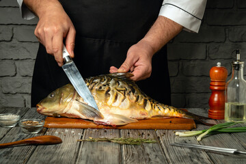 A chef skillfully fillets a fresh fish on a wooden cutting board in a modern kitchen. Herbs,...