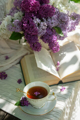 A bouquet of lilacs on the table and a cup of tea.