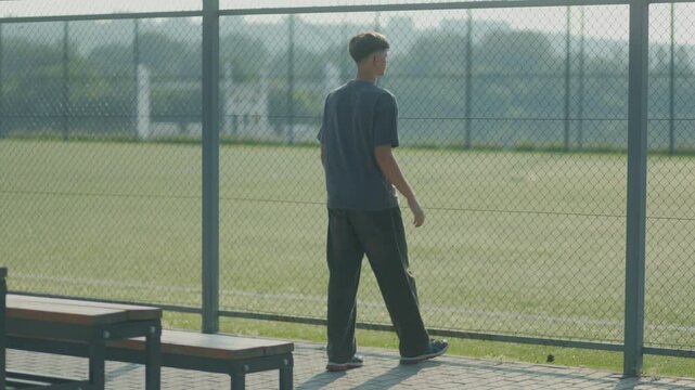 Teen Looks Out Over Empty Field from Behind Fence at School