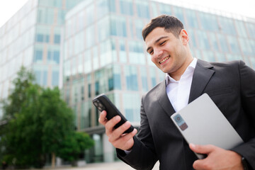 Fototapeta premium Business professional enjoys a moment of connection outside a modern office building while checking messages on his smartphone