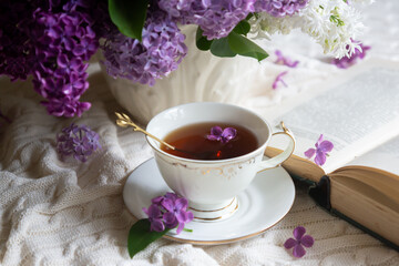 A bouquet of lilacs on the table and a cup of tea.