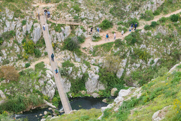 Matera, Italy. People cross a Tibetan bridge over the Gravina river along path 406 in the Murgia Materana Park, beneath the historic Sassi di Matera in southern Italy. 2025-04-18.