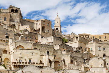 Matera, Italy. Scenic view of the historic center of the Sassi di Matera, Italy, with ancient stone houses and the bell tower of Matera Cathedral under a bright blue sky.