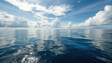 Tranquil ocean surface with clear blue sky and scattered clouds  