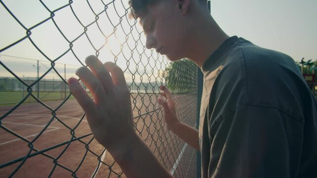 Teen Standing by Fence at Sunset Reflecting Over School Field