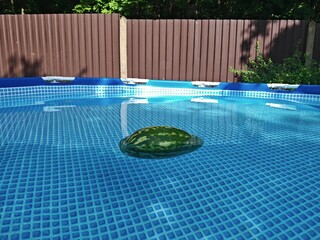 The blue PVC frame round pool is filled with clean water. A watermelon is floating and cooling in...