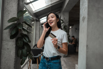 Fototapeta premium Happy asian woman holding credit card and using smartphone for online shopping