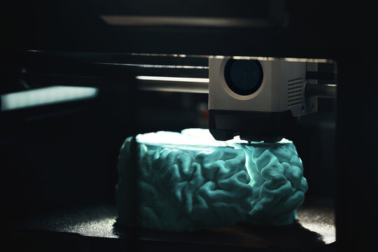 3D printing of a cyan human brain model &ndash; dark low-light view of FDM printer layer-by-layer fabrication for neuroscience, medical research and rapid prototyping.