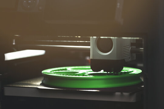 3D printing of a green planetary gear model &ndash; low-light view of FDM printer fabricating mechanical component for engineering rapid prototyping and additive manufacturing.
