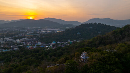 Aerial view of Sunset above Khao Rang viewpoint. view of a town nestled among lush green mountains at sunset, with a Pavilion structure perched on the hillside at Phuket town at Dusk