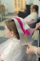 A little girl has her hair dyed bright pink in a beauty salon.