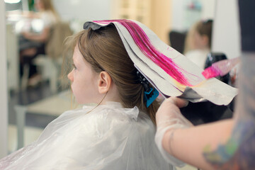 A little girl has her hair dyed bright pink in a beauty salon.
