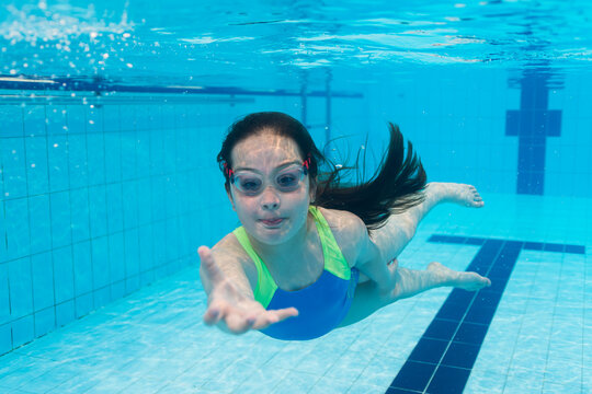 Amazing underwater photo: a happy girl gracefully swims towards the camera in a pool, reaching her hand out. Sports and the joy of movement.