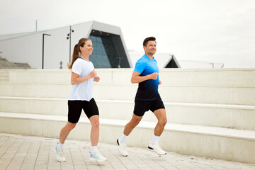 Couple enjoying a brisk morning jog in a modern urban park with captivating architecture in the...