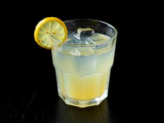 Refreshing lemon cocktail with ice cubes and lemon slice on black background