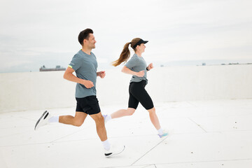 Couple enjoying a lively run on a rooftop under a cloudy sky in an urban setting during early...