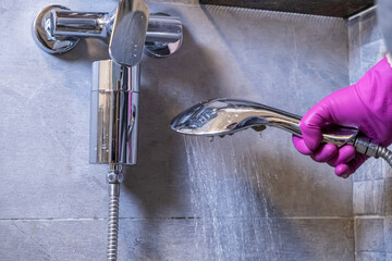 Hand in a pink glove holds a running chrome shower head with an active water filter, promoting pure...