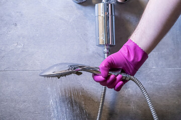Pink gloved hand holds a running shower head with a water filter system, illustrating home water...