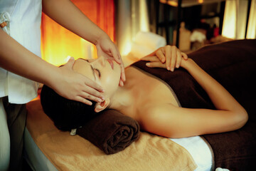 Caucasian woman enjoying relaxing anti-stress head massage and pampering facial beauty skin recreation leisure in warm candle lighting ambient salon spa in luxury resort or hotel. Quiescent