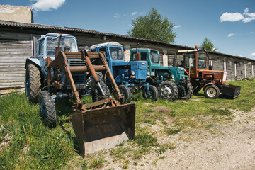 Old Soviet Tractors Parked in Front of Rural Garages on a Sunny Day