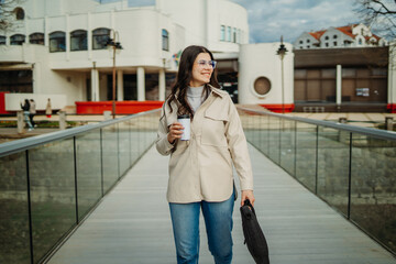 Young caucasian woman walk home from work drink coffee and use smartphone	
