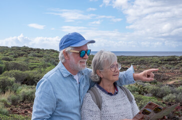 Carefree senior couple in walking day in countryside along the seacoast looking at the horizon over water. Elderly smiling retirees enjoying healthy lifestyle and vacation in nature