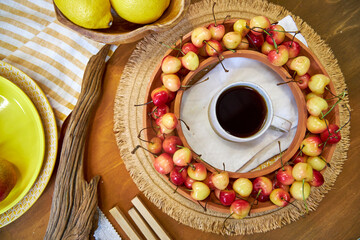 Top view flat lay of a summer-inspired moodboard and color palette arranged on a rustic wooden surface. The scene includes vibrant yellow plates, fresh lemons, ripe cherries, fabric swatches, 