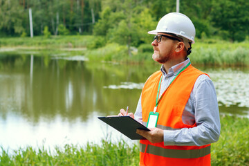 Male forestry inspector studying the condition of trees near water in the forest. Ecologist's work. Conducting environmental monitoring.