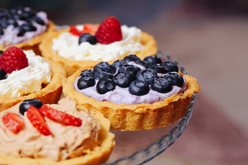 Mini tartlets with whipped cream. Mixed berry toppings including blueberries and strawberries. Assorted sweet pastries on glass plate. Dessert buffet or party treat idea.