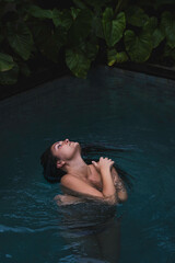A woman with braids enjoying in a pool, surrounded by lush tropical leaves in a serene and intimate moment in Ubud, Bali, Indonesia