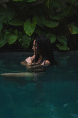 A woman with braids enjoying in a pool, surrounded by lush tropical leaves in a serene and intimate moment in Ubud, Bali, Indonesia